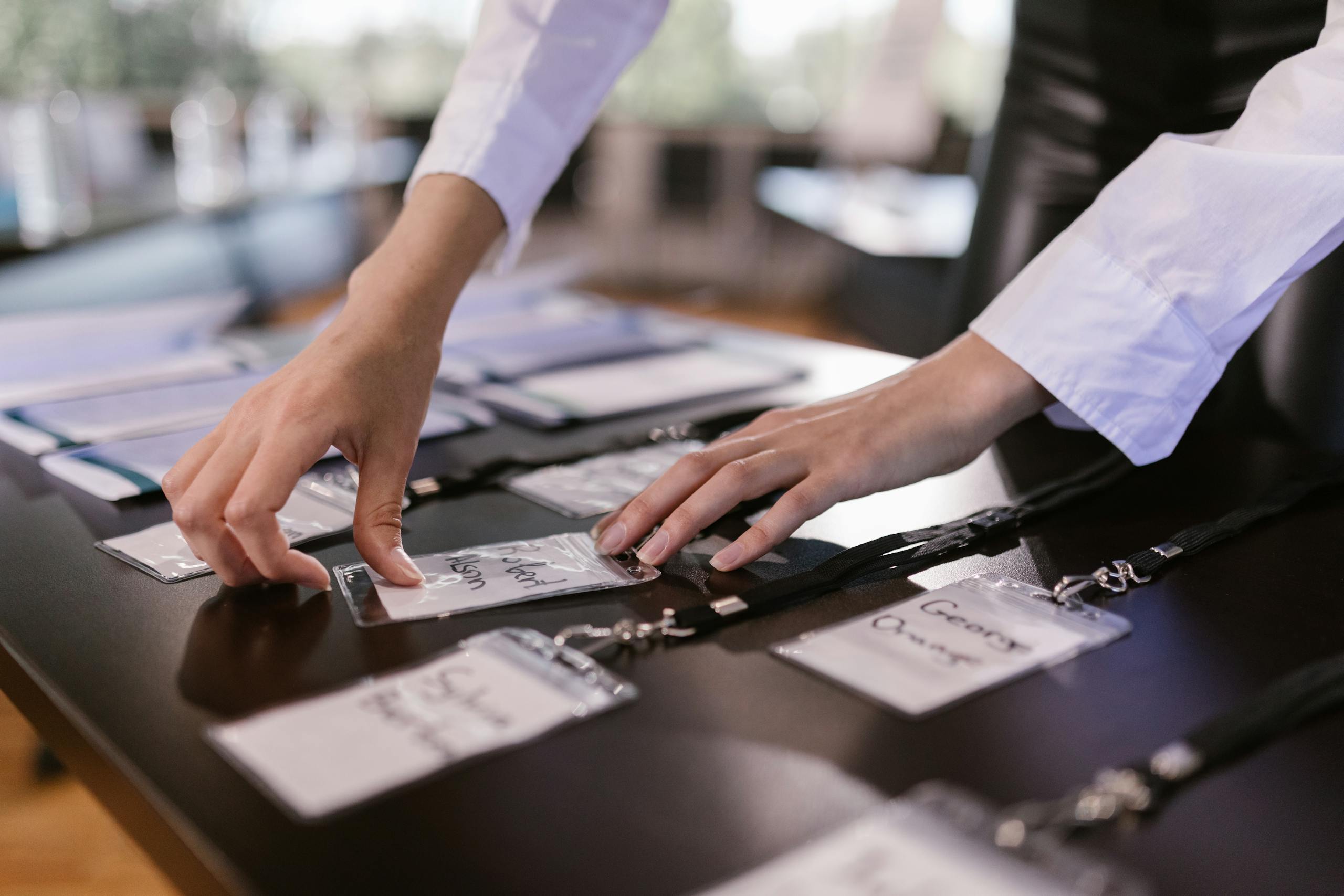 Close-up of hands arranging name tags on a conference table, preparing for a corporate event.