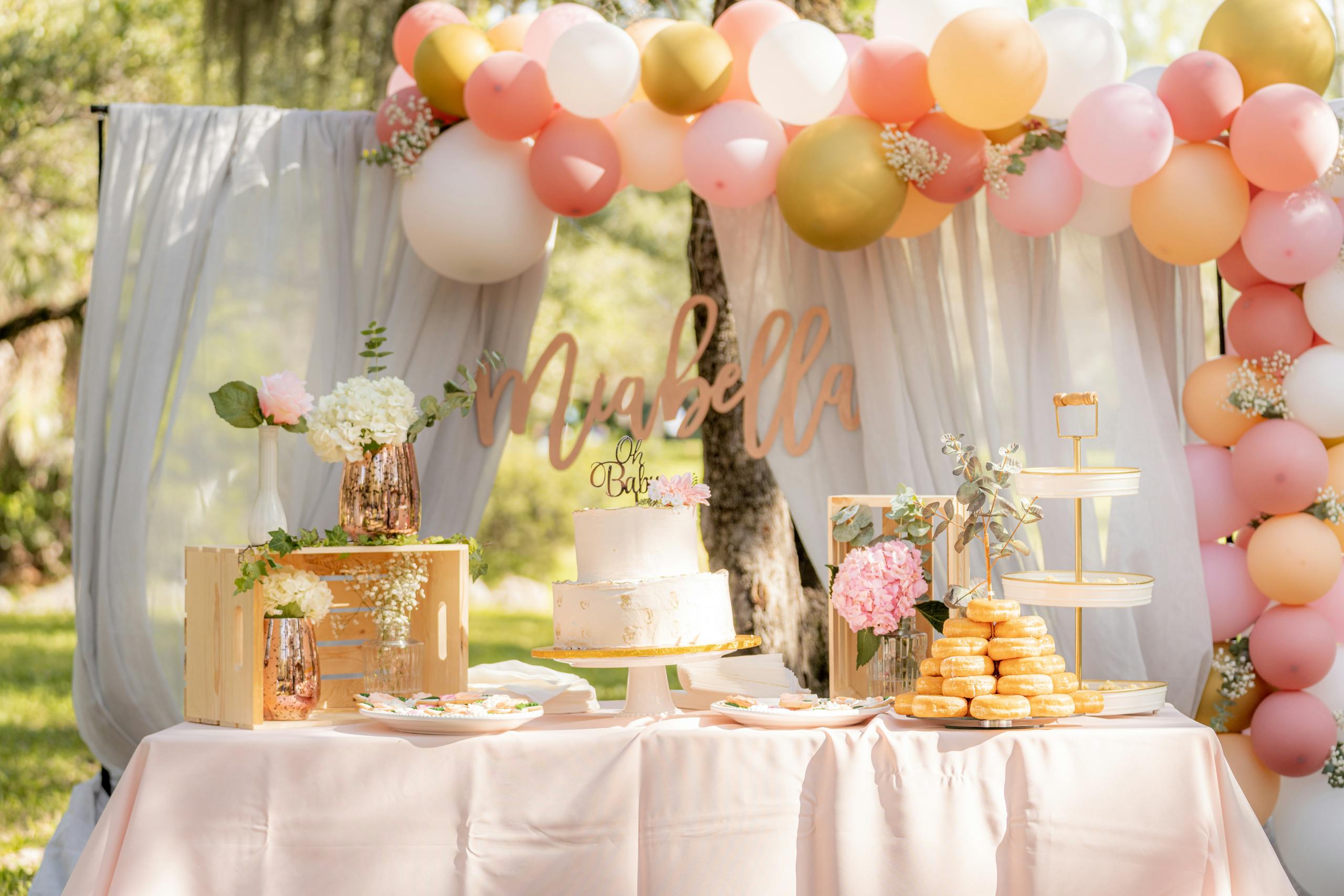 Delightful baby shower table with cake, balloons, and dessert display in an outdoor garden setting.