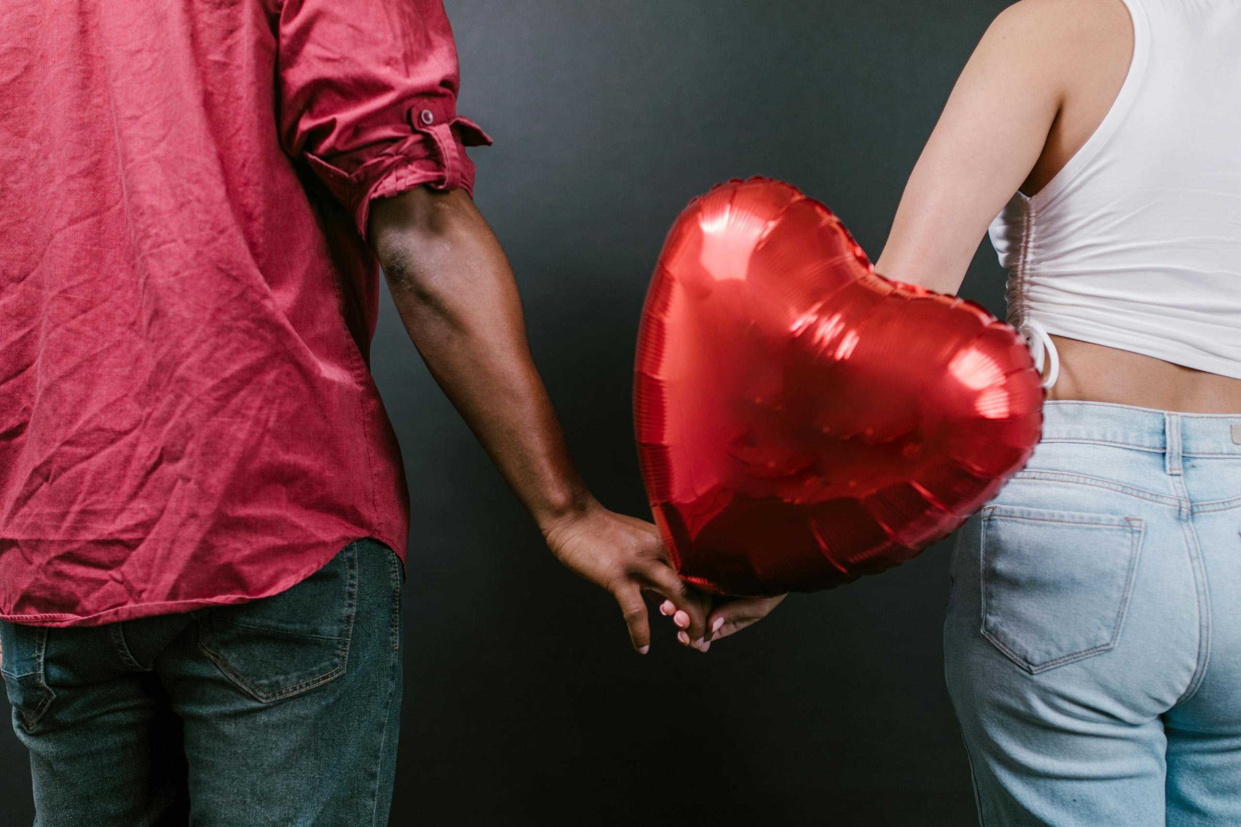 A couple holding hands with a red heart-shaped balloon symbolizing love and togetherness.
