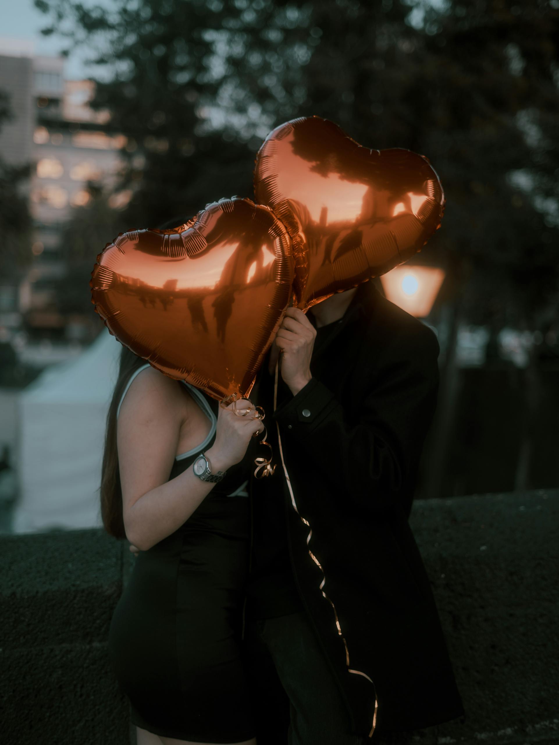 A couple holding heart-shaped balloons embracing in an outdoor setting with a romantic vibe.
