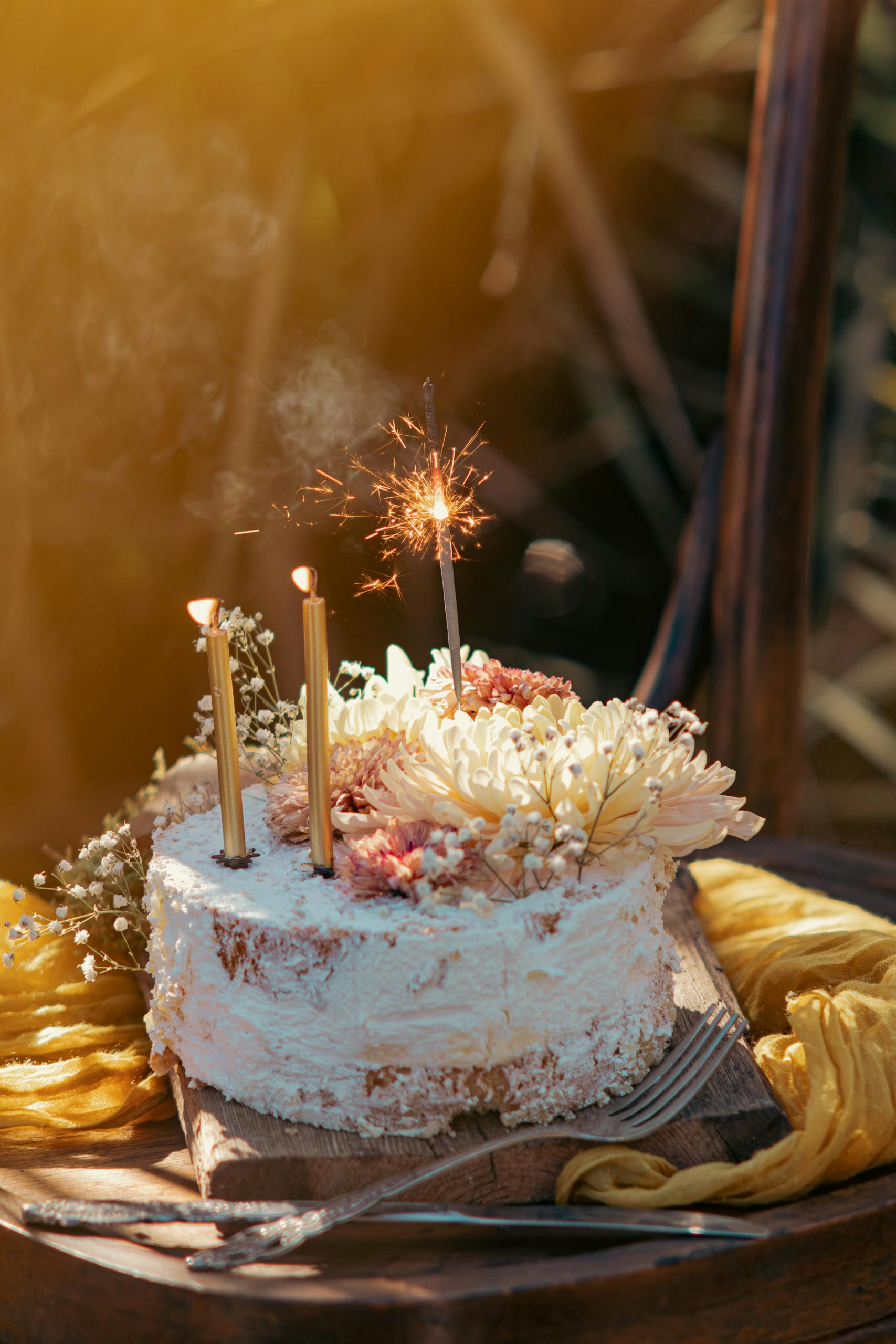 A rustic cake adorned with flowers and sparklers, set outdoors in beautiful autumn light.