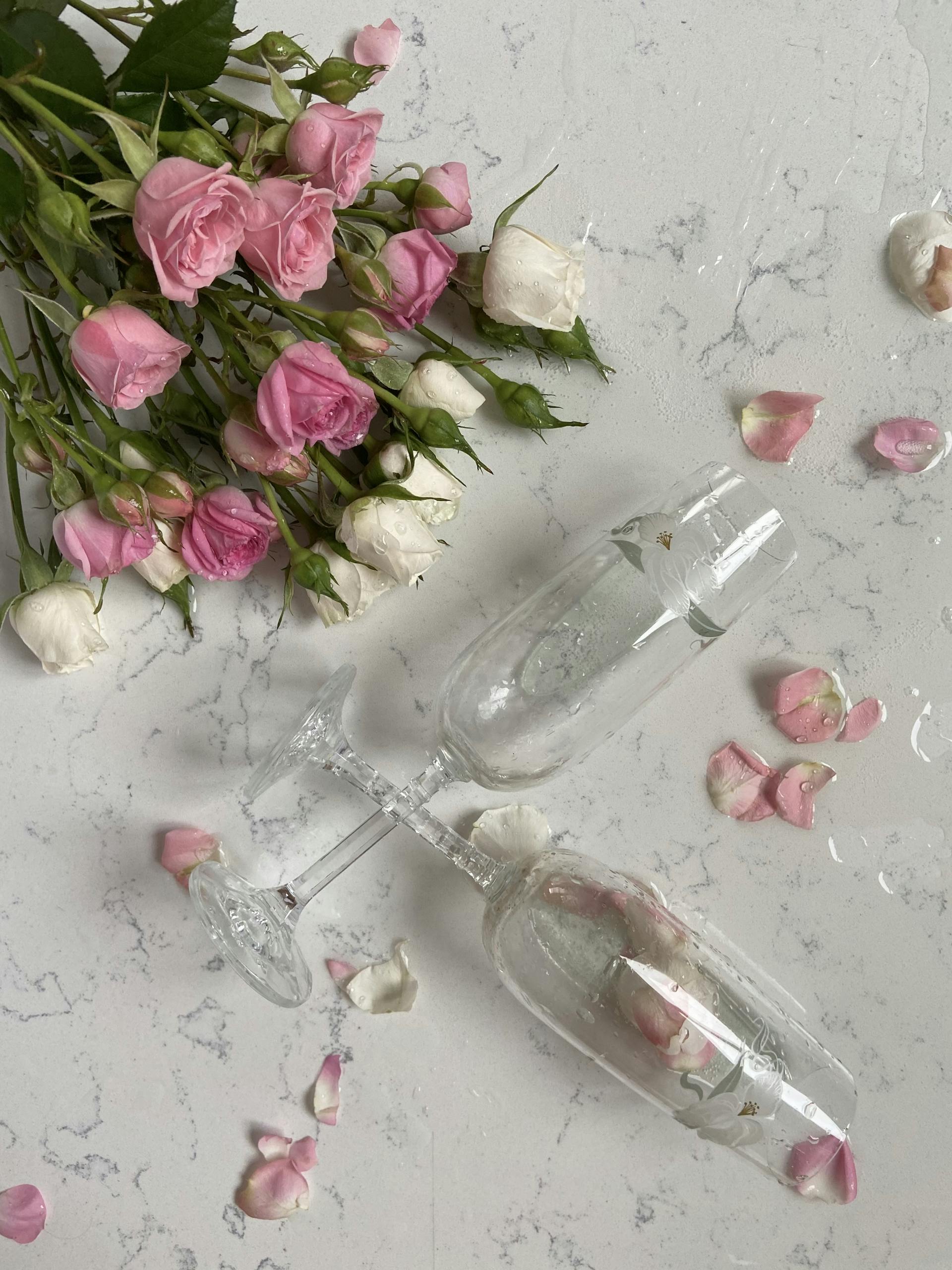 Delicate pink and white roses with champagne glasses on a marble surface.