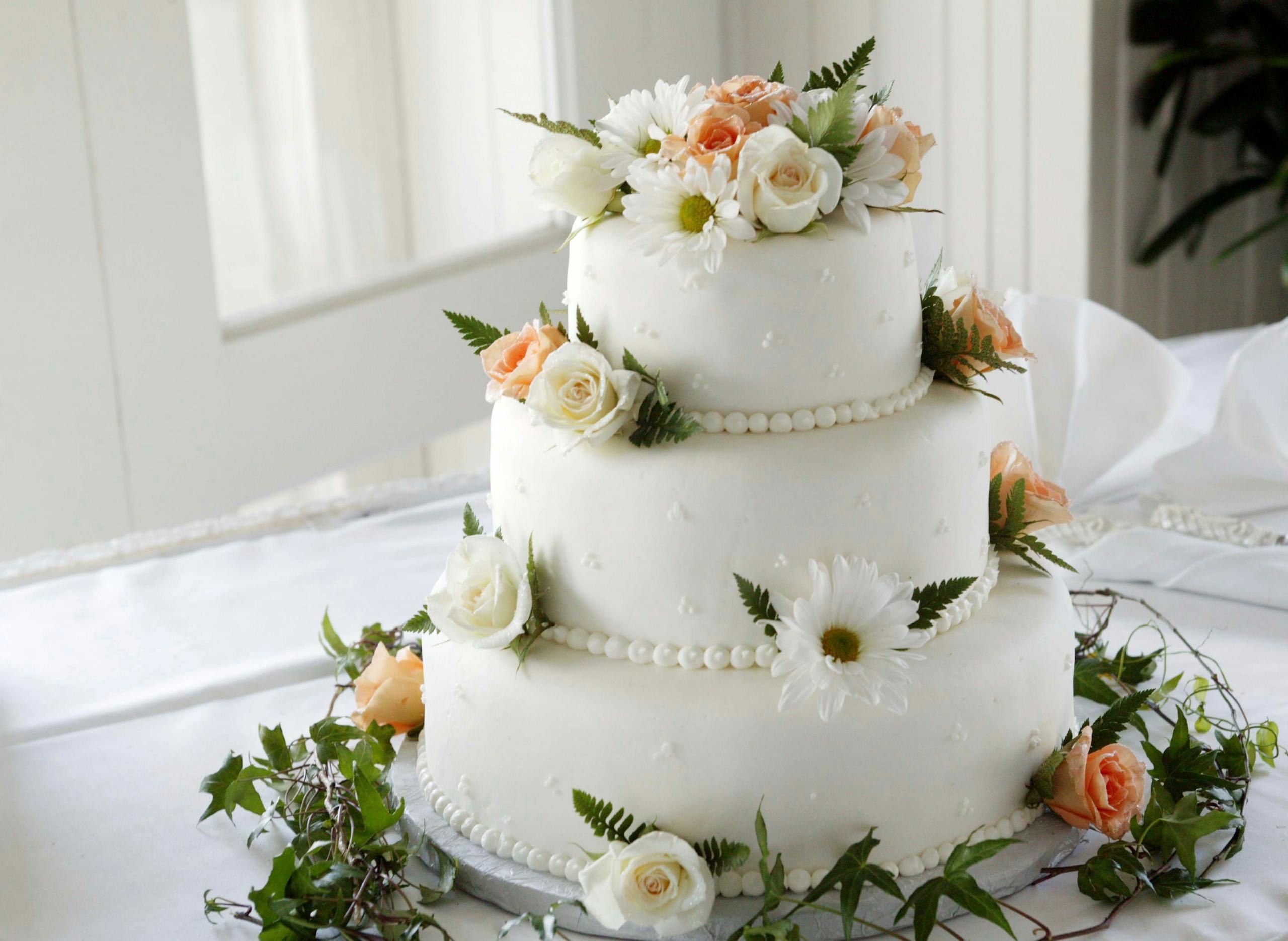 Elegant white wedding cake adorned with fresh roses and daisies, perfect for a romantic celebration.