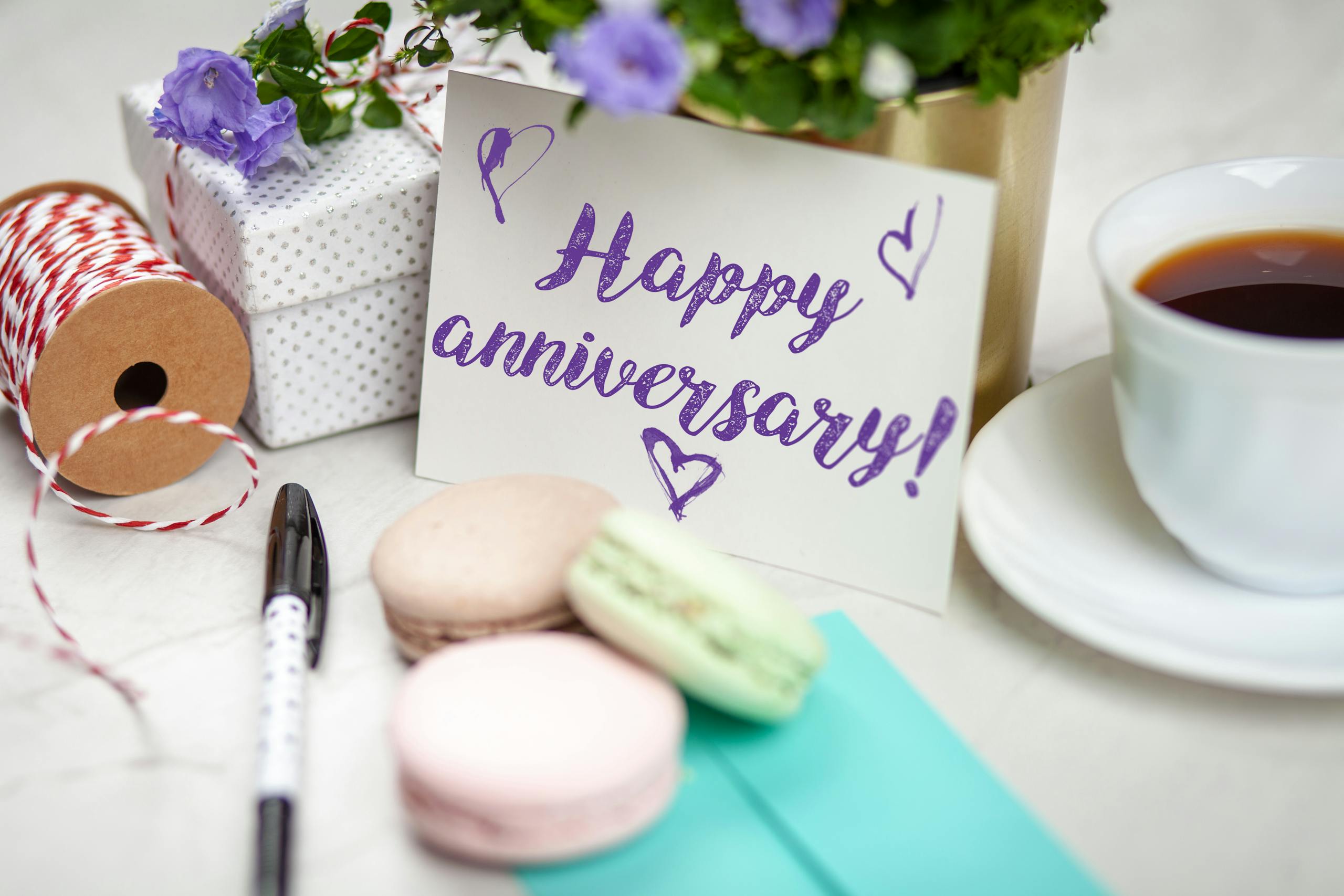 Happy anniversary card with flowers, gift, macarons, and coffee on a table.