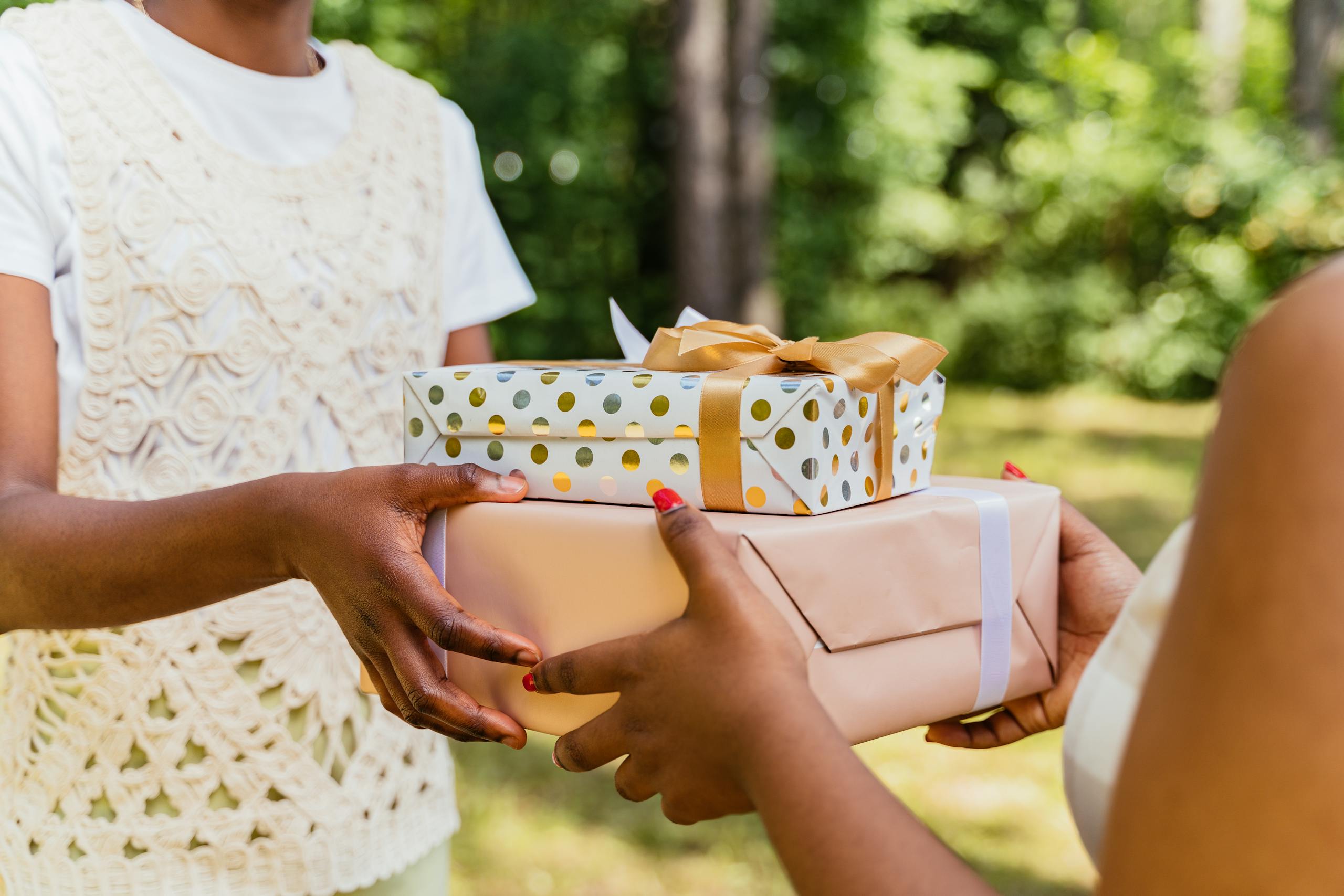 Two individuals exchanging colorfully wrapped gift boxes in a lush outdoor setting, symbolizing celebration.